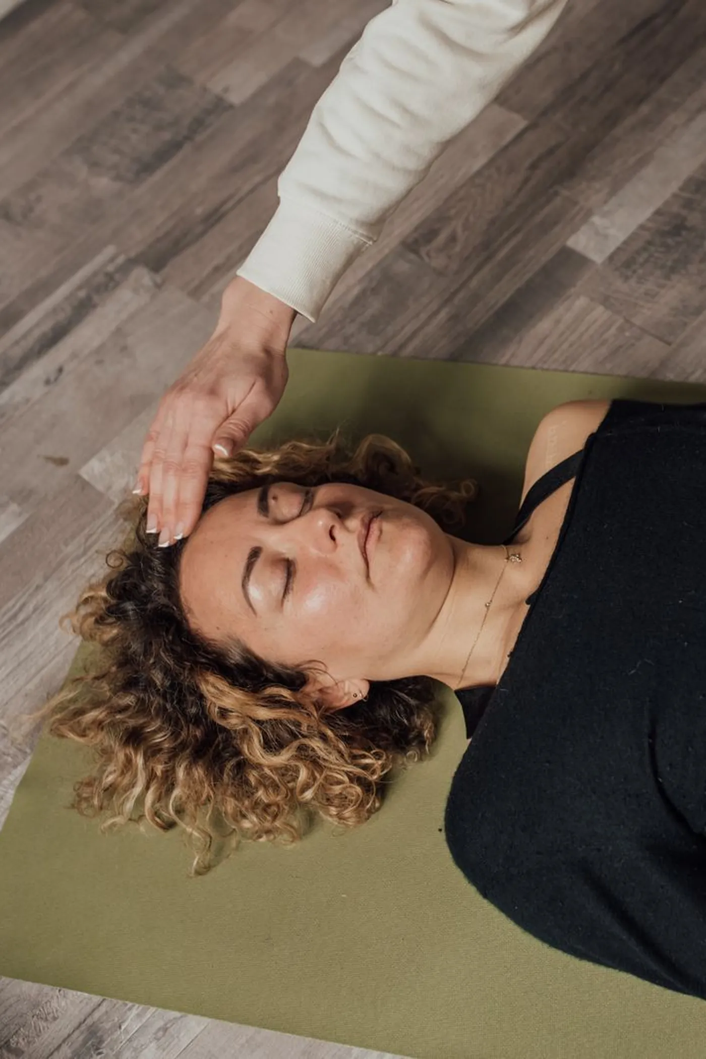 Vue de dessus : les mains du praticien au-dessus de la tête et du buste d'une personne allongée et habillée