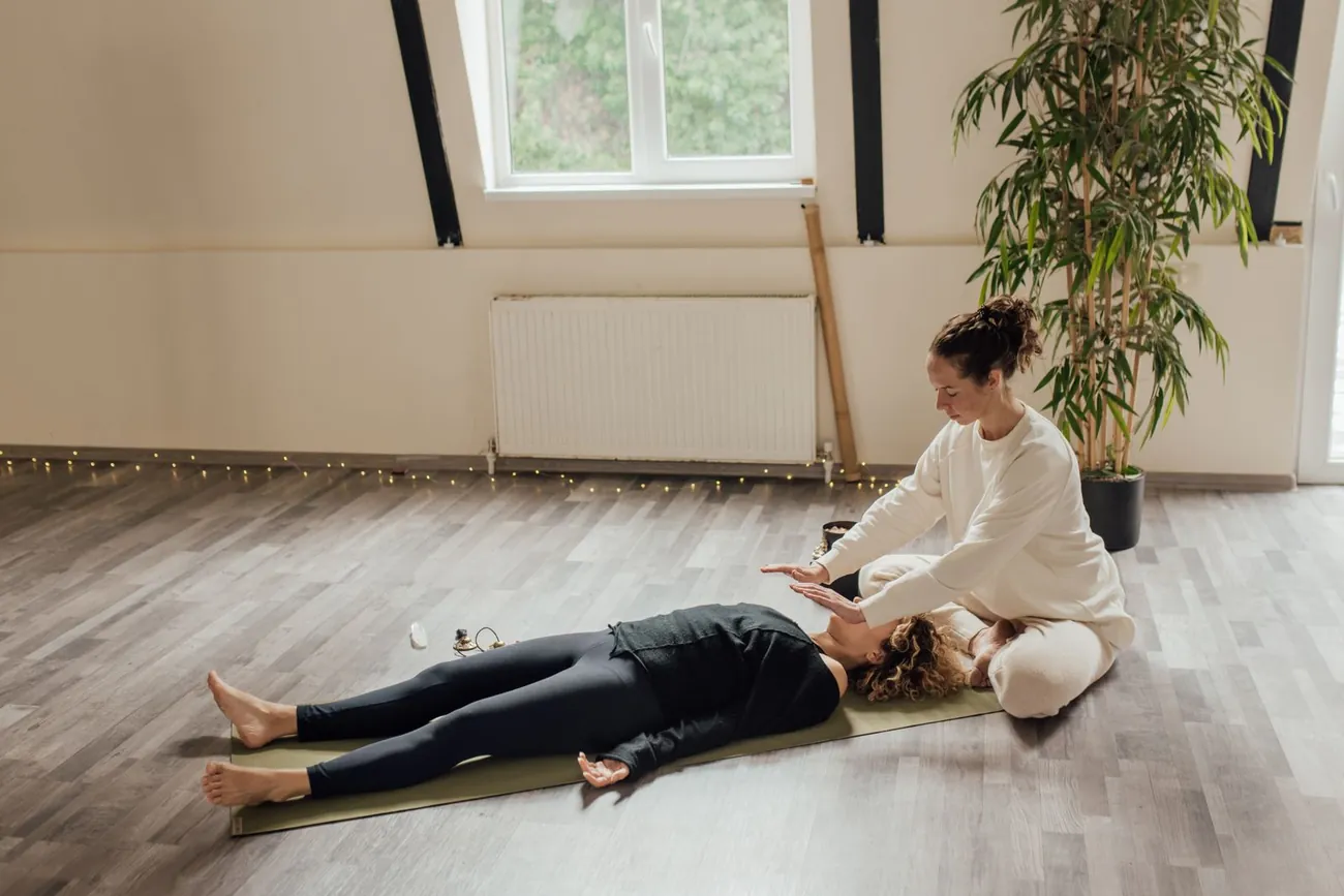 Séance au sol dans une pièce claire : la personne est allongée et habillée, le praticien est assis à côté d'elle